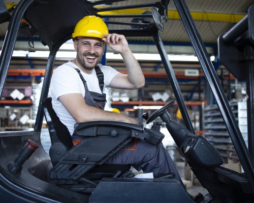 Portrait of smiling professional forklift driver in factory's warehouse.
